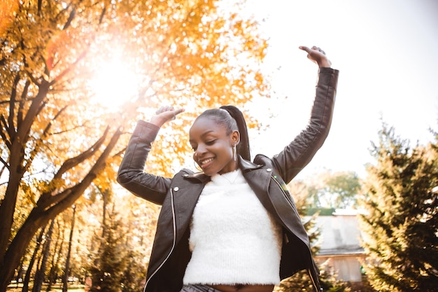 African american woman with dark hair dancing having fun outside autumn city park blur yellow leaves