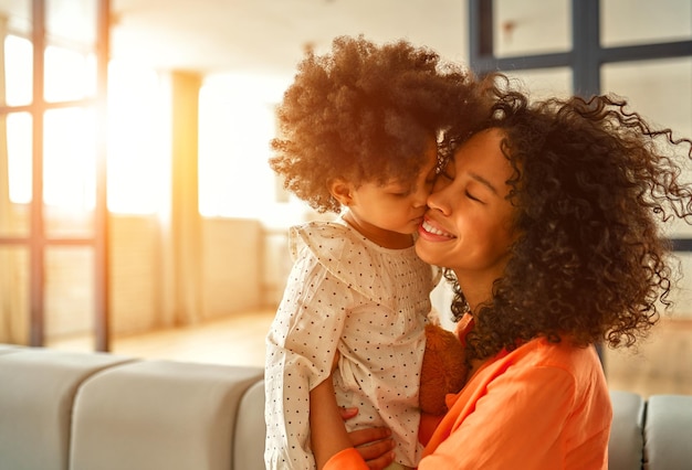 照片非裔美国妇女与她的小女儿卷曲蓬松的头发在客厅坐在沙发上,轻轻拥抱在家里