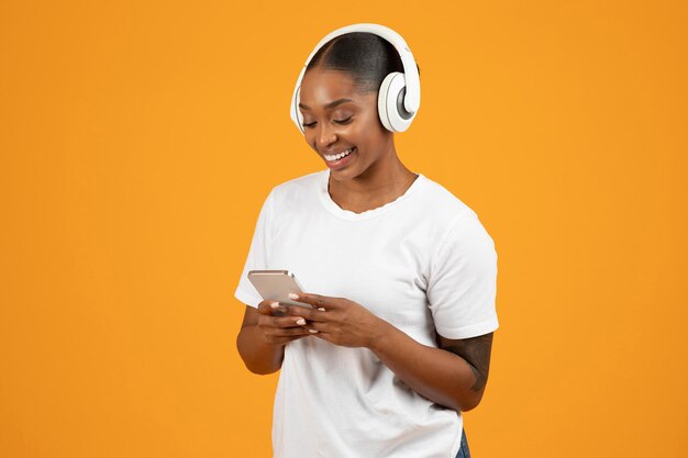 African american woman with mobile phone in headphones orange studio