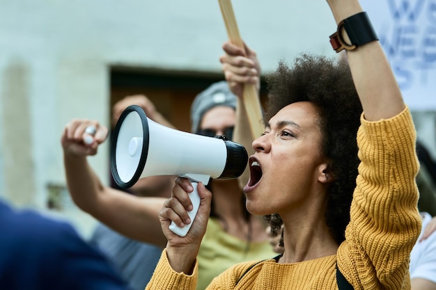 African American woman with raised fist shouting through megaphone on antiracism protest