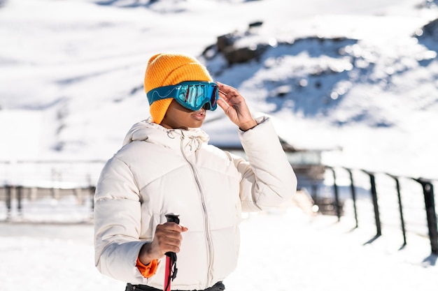 冬の間に雪山に立っているスキーストックを持つアフリカ系アメリカ人の女性