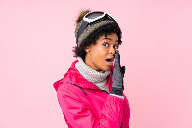 African American woman with snow goggles over pink wall