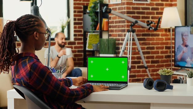 African american woman working with greenscreen display on laptop, using blank copy space background. Manager analyzing isolated chroma key and mock up template on computer. Tripod shot.