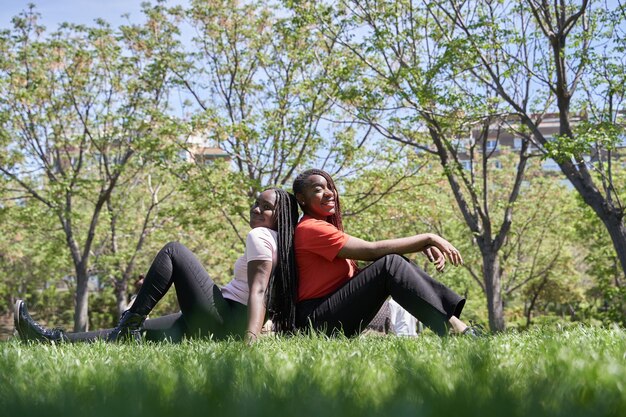 芝生の公園に背中合わせに座っているアフリカ系アメリカ人の女性