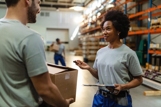 african american worker talking to her male colleague while working together in distribution warehouse