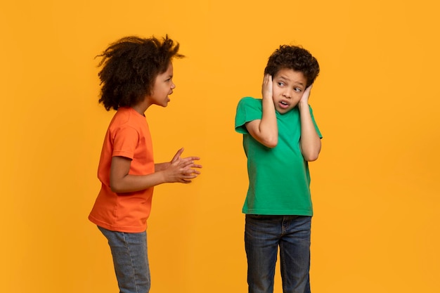 Photo african american young girl appears to be talking animatedly to a boy who is covering his ears with