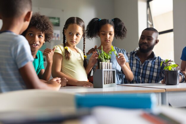 Photo african american young male teacher looking at multiracial elementary students discussing on plants