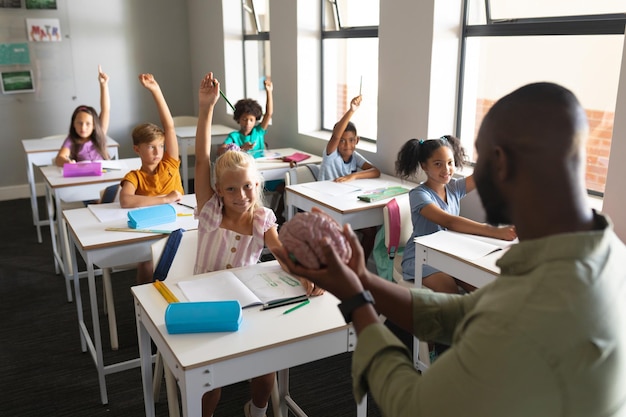 African american young male teacher showing brain model to multiracial students with hand raised. unaltered, education, learning, childhood, occupation, teaching, science and school concept.