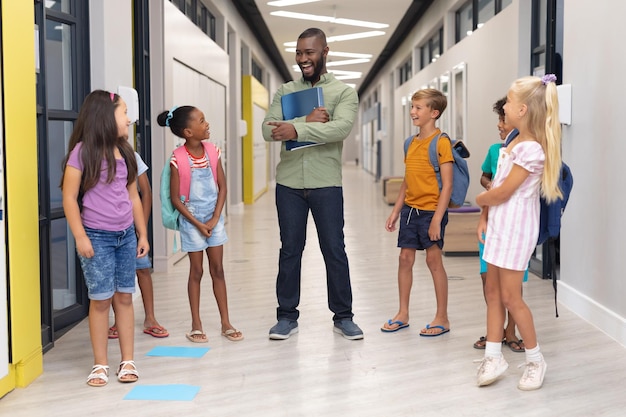 Photo african american young male teacher talking to multiracial elementary students standing in corridor