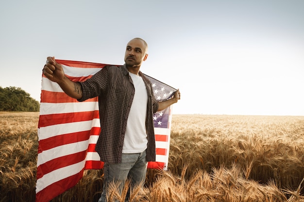 African american young man holding usa national flag through wheat field