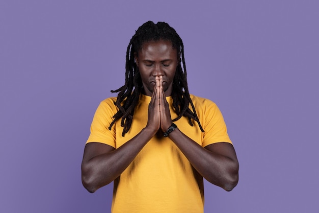 African american young man praying with closed eyes on purple