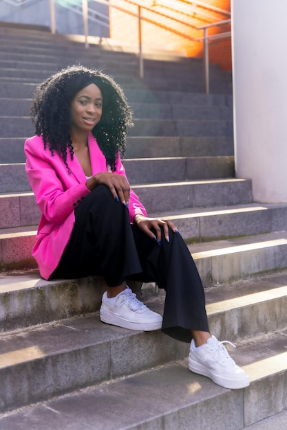 African american young woman in the city portrait of young woman in pink jacket sitting smiling