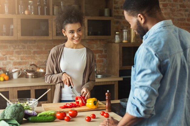 African american young woman looking at boyfriend while cooking salad at kitchen. Family preparing dinner