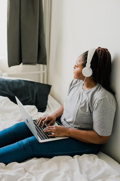 African american young woman using laptop with headphones on bed technologies and communication and