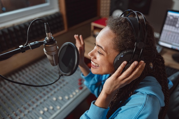 Photo african anchorwoman with headphones talking into professional microphone in sound recording or broadcasting studio