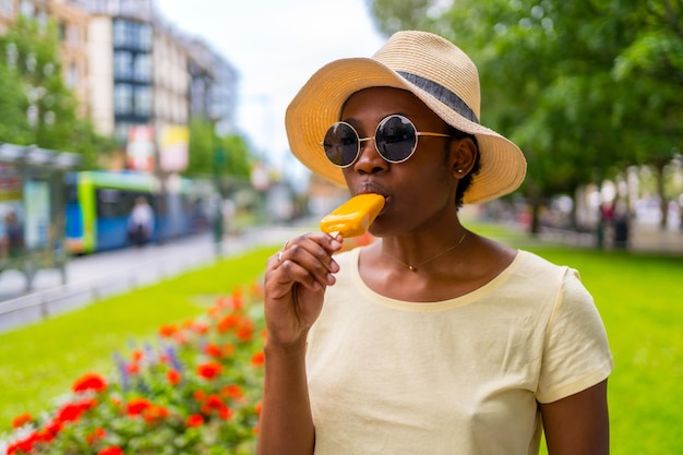 African black ethnicity woman eating a mango ice cream in the city in summer