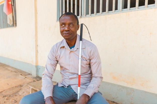 Foto un cieco africano con un bastone si siede su una panchina