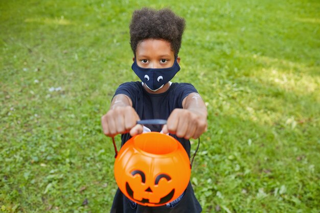 African boy in Halloween costume holding pumpkin basket and asking for treats while standing outdoors