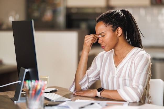 African business woman looking worried while working on computer from her home office.