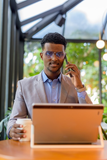 African businessman at coffee shop using laptop computer and talking on phone