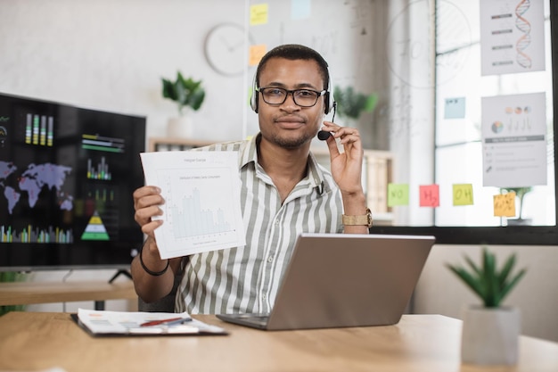 African businessman in eyeglasses using laptop for video conference at office