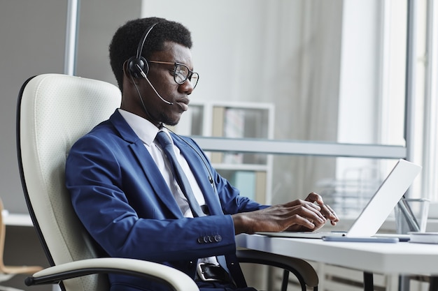 African businessman in headphones typing on laptop computer at his workplace he working in call centre