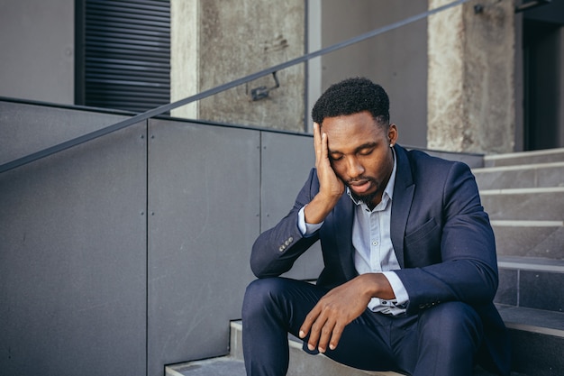 African businessman sitting frustrated on the stairs depressed by the results of his work, holding hands behind his head