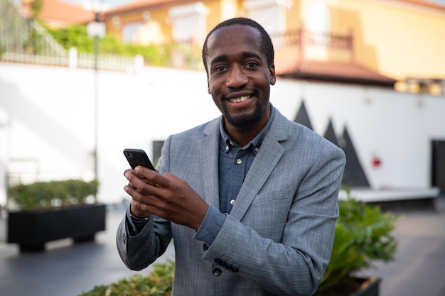 African businessman smiles as he uses his smartphone. Happy entrepreneur. Positive worker with a content facial expression