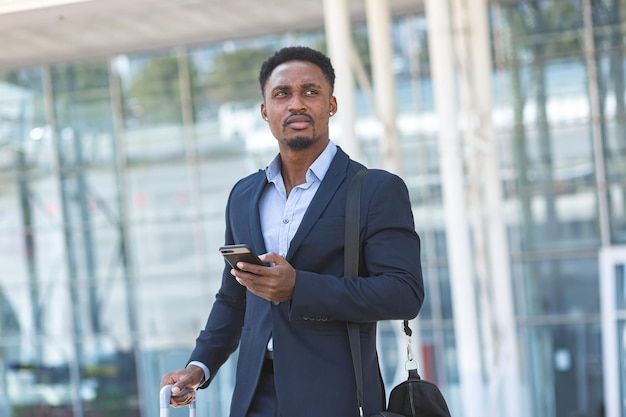 African businessman traveling near airport with suitcase calling taxi using mobile app