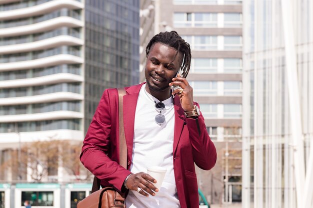 african businessman walks through the city talking on the phone with a coffee in his hand