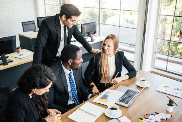 African businessmen sit among Caucasian colleagues looking on laptop at an internal business group meeting. Diversity of businesspeople cooperation.