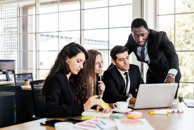 African businessmen standing in the back of Caucasian colleagues with smiles looking on laptop