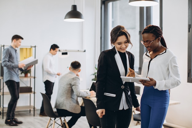 African and Caucasian White businesswomen using a tablet with interracial group of business men