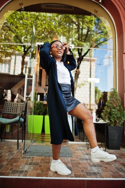 African chic business girl in coat and sunglasses. Fashionable street portrait of african american woman.