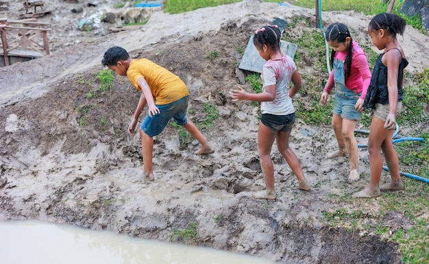 African child and asian girl playing in puddle mud together at outdoor summer camp learning