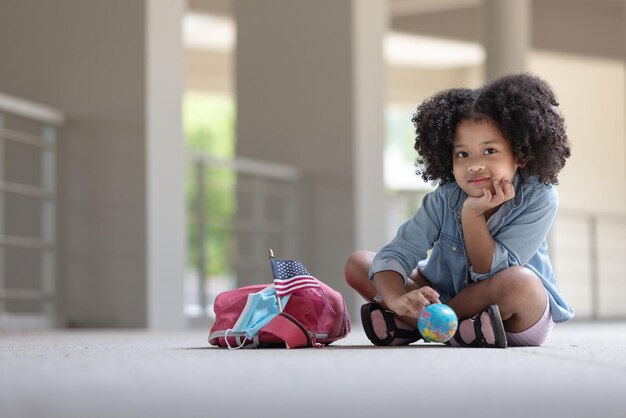 Photo african children curly hair sitting under building with globe on hand looking at camera