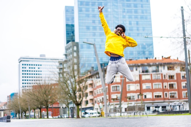 Photo african cool man jumping happily while listening to music outdoors