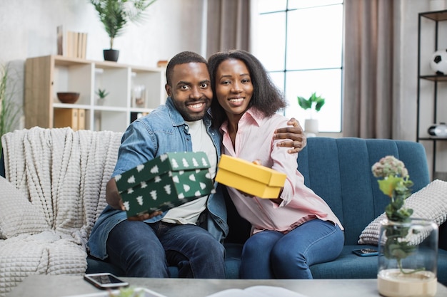 Photo african couple holding gift boxes and smiling on camera