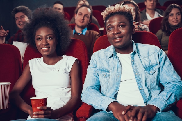 African couple with popcorn watching movie in cinema