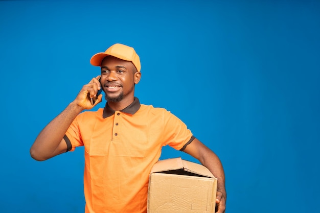 African delivery man making calls with his cellphone isolated over blue background