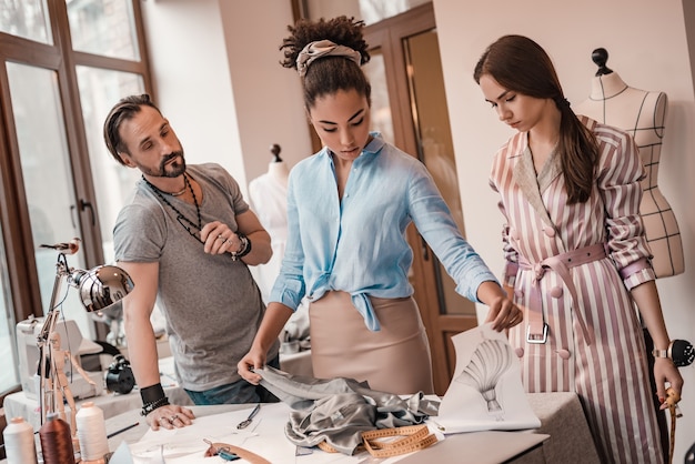 African designer touches material. Group of three people at design studio. Man and two women are making decigion