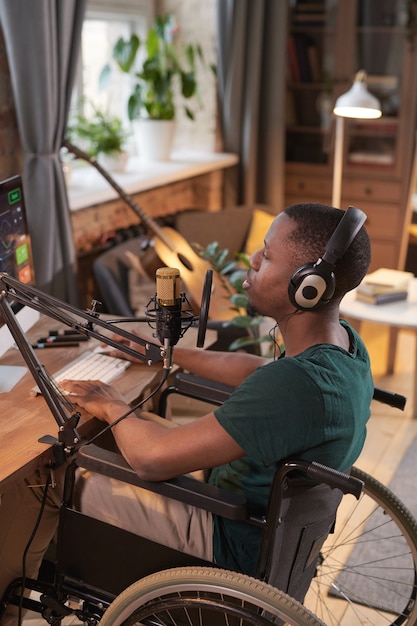 African disabled man in wheelchair sitting at the table and recording a new song at home