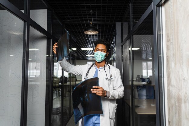 Африканский врач изучает рентгеновские снимки в медицинской клинике Черный студент в медицинской маске изучает и смотрит на компьютерную томографию