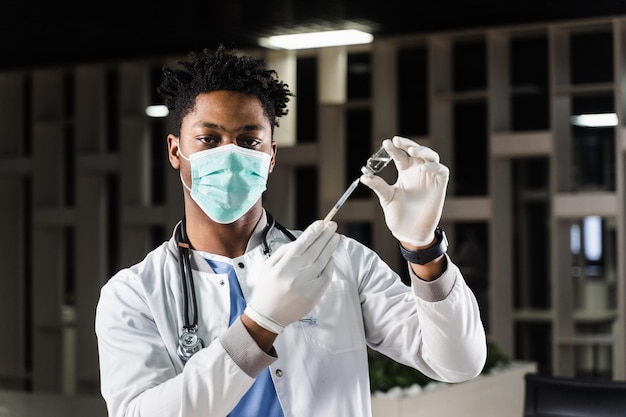 의료 마스크를 쓴 아프리카 의사가 코로나바이러스 covid19 백신을 주사할 준비를 하고 백신 접종을 위해 주사기가 있는 흰색 의료 가운을 입은 흑인 의사