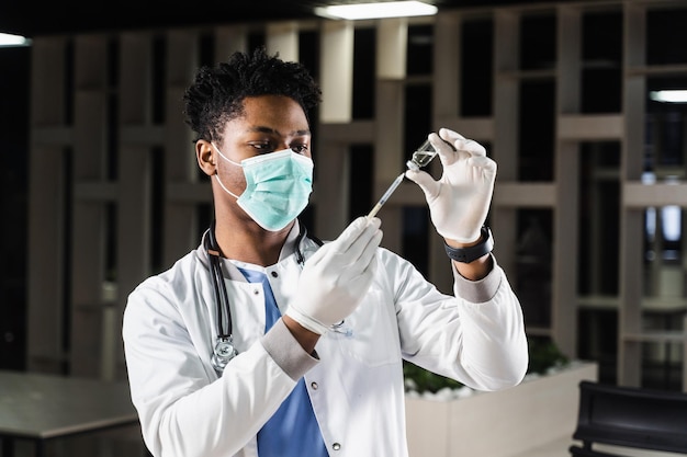 African doctor in a medical mask prepares to inject coronavirus covid19 vaccine Black doctor in white medical robe with syringe for making vaccination