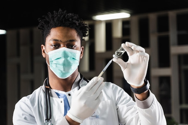 African doctor in a medical mask prepares to inject coronavirus covid19 vaccine Black doctor in white medical robe with syringe for making vaccination