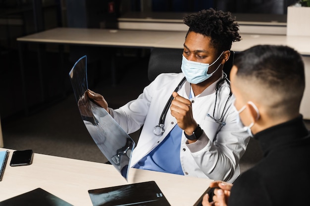 African doctor show xray asian patient black surgeon analyzing\
x ray and diagnosis patient in medical clinic