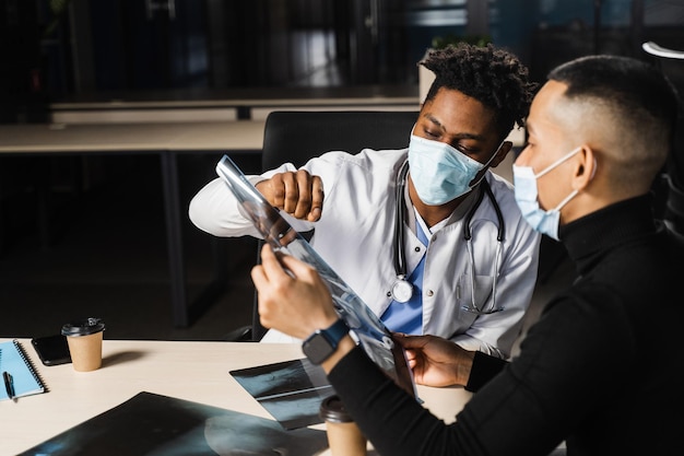 Африканский врач показывает рентген азиатскому пациенту Пневмония и плеврит Черный хирург анализирует рентген и ставит диагноз пациенту в медицинской клинике
