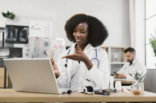 African doctor showing pills to patient during video call