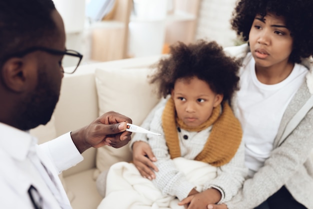 African doctor takes temperature of sick kid with flu.